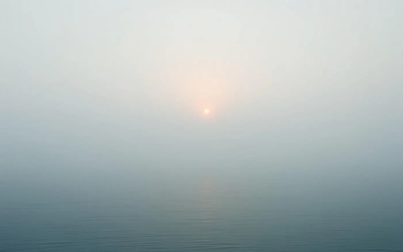 Amanhecer suave sobre água parada, com névoa